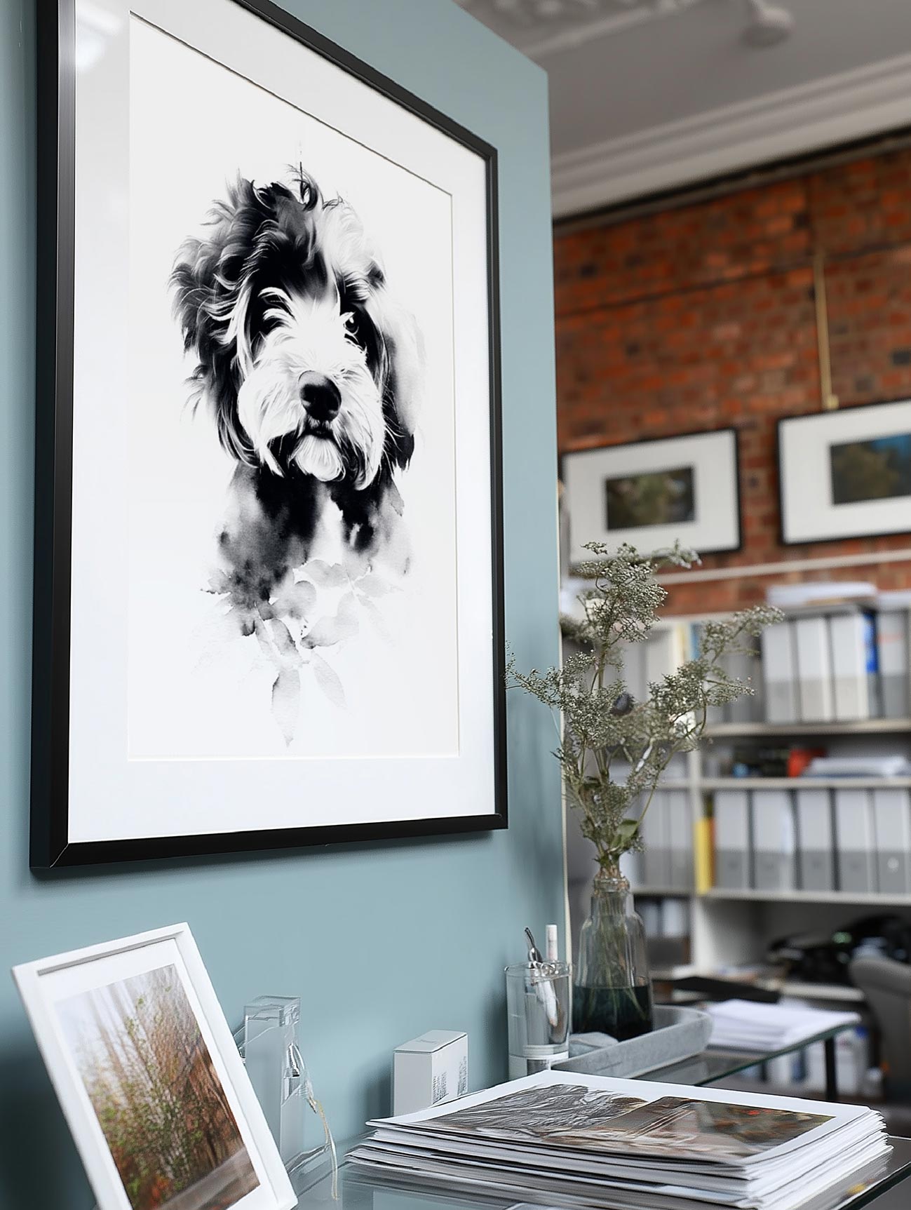 Framed black and white pet portrait on a light blue wall with a bookshelf in the background.